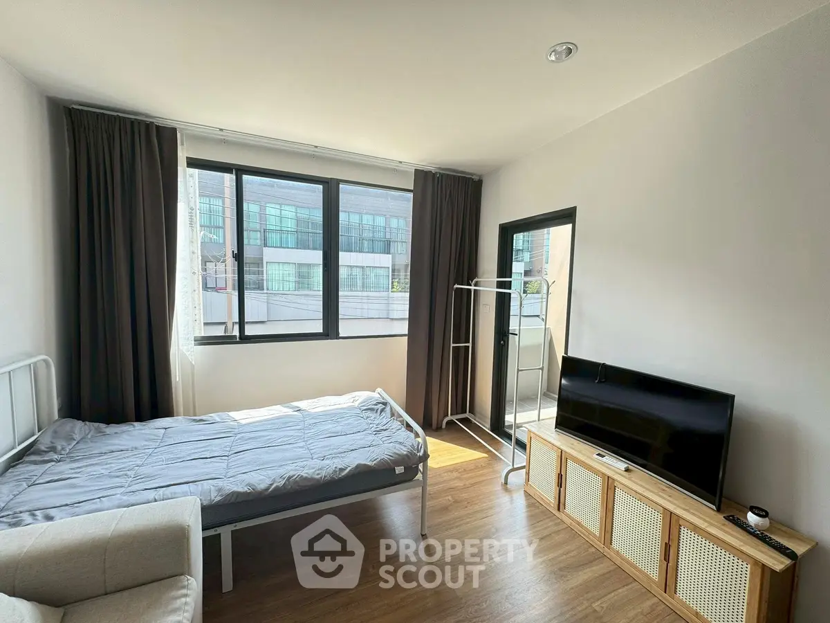 Modern bedroom with large windows and natural light, featuring a bed, TV, and minimalistic decor.