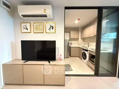 Modern living room with TV and kitchen featuring washing machine and sleek cabinetry.