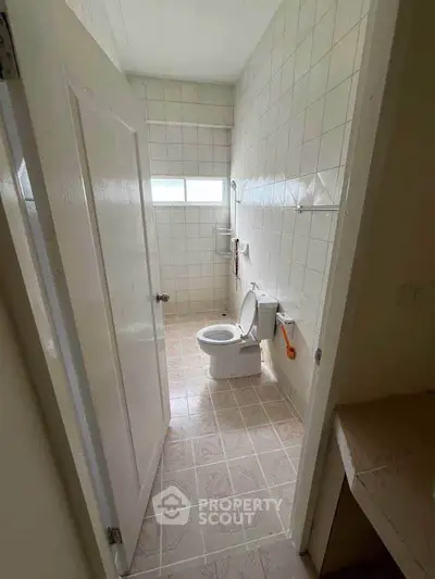 Compact bathroom with tiled walls and floor, featuring a toilet and window for natural light.