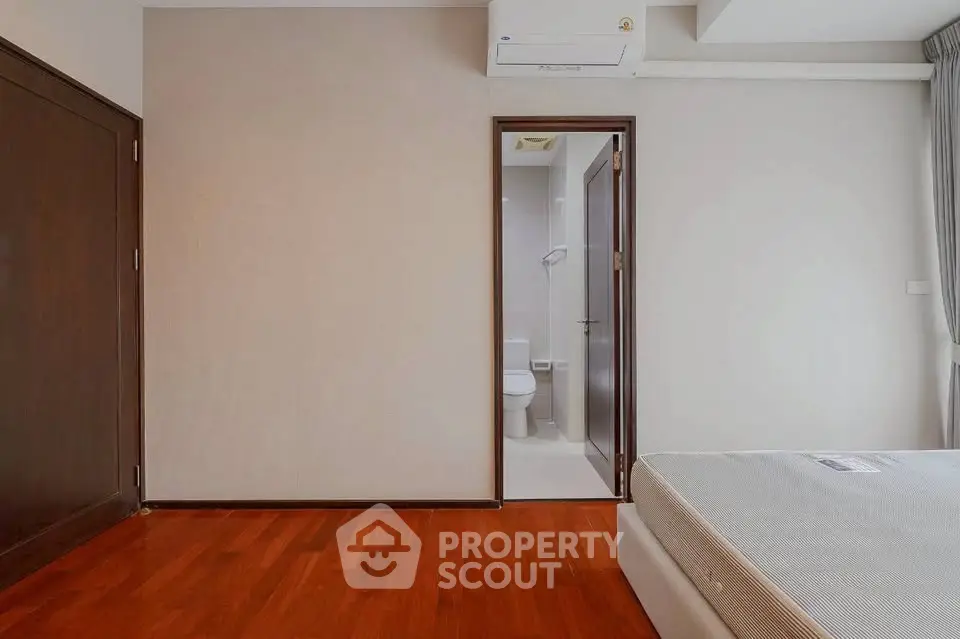Spacious bedroom with wooden flooring and ensuite bathroom in modern apartment.