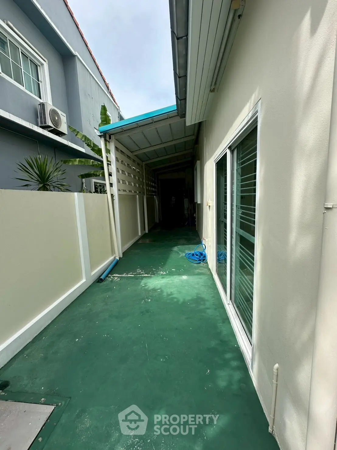 Charming side pathway of a modern home with green flooring and sliding glass doors.