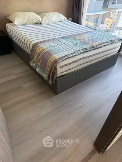 Modern bedroom with stylish bed and large window offering natural light and urban view.