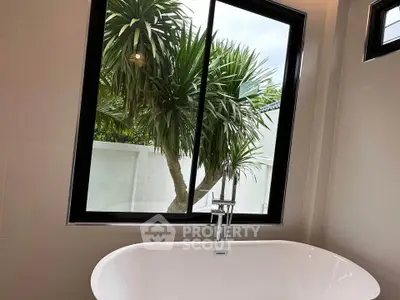 Luxurious bathroom with a modern bathtub and a scenic view of lush greenery through a large window.
