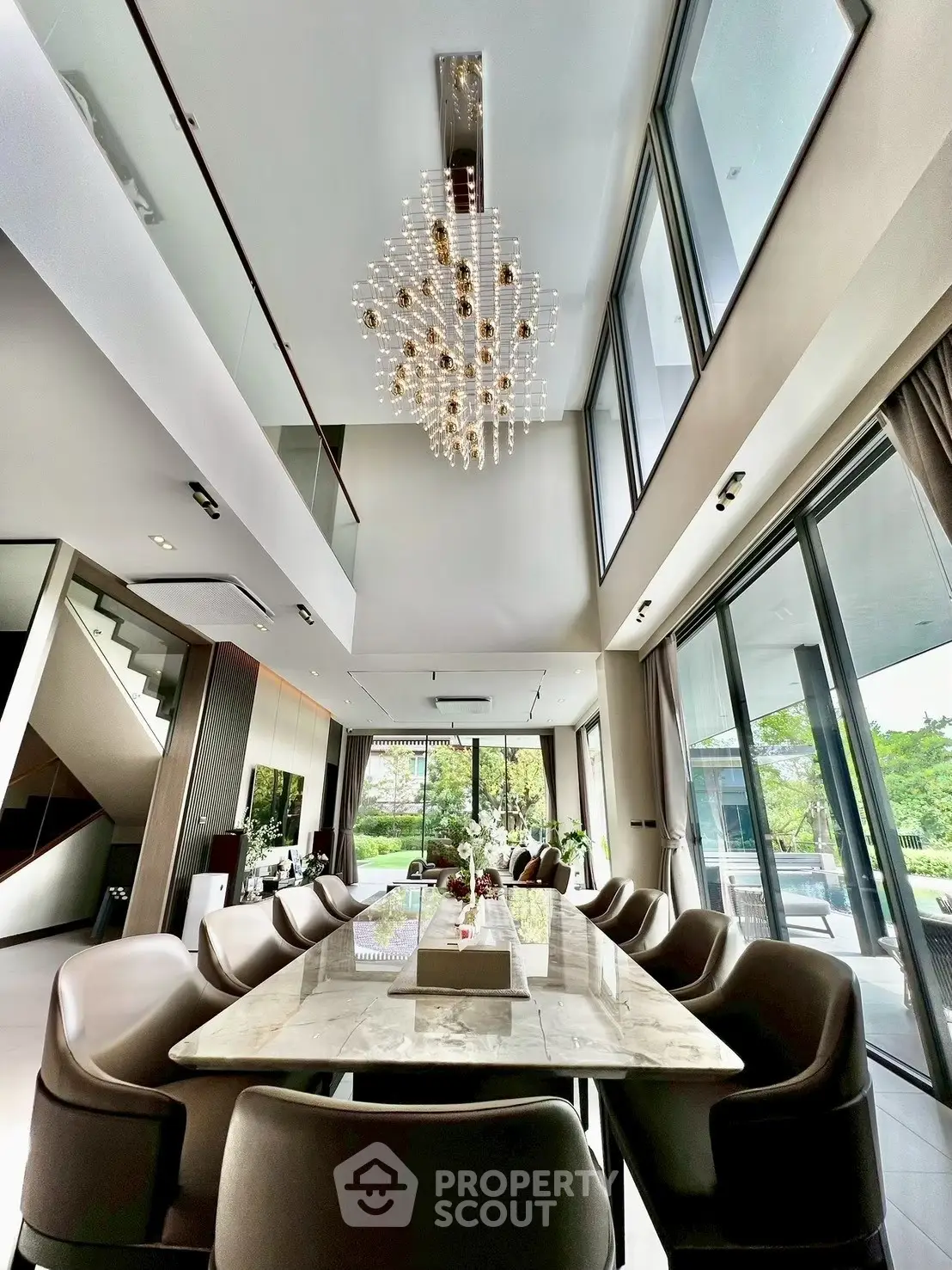 Luxurious dining area with high ceilings, elegant chandelier, and large windows offering garden views.