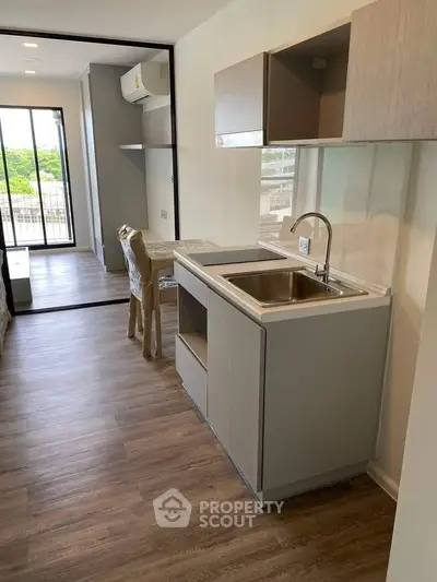 Modern apartment kitchen with sleek cabinetry and open layout, featuring a view of the living area and balcony.