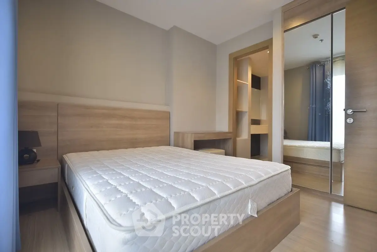 Modern bedroom with wooden furniture and large mirror reflecting natural light.