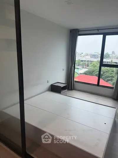 Modern bedroom with large window offering city view, minimalist design and ample natural light.