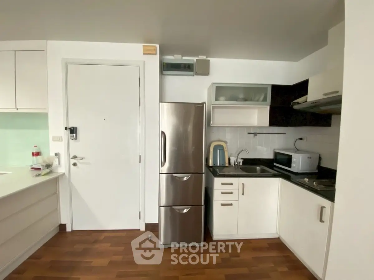 Modern kitchen with stainless steel fridge and sleek cabinetry in a cozy apartment.