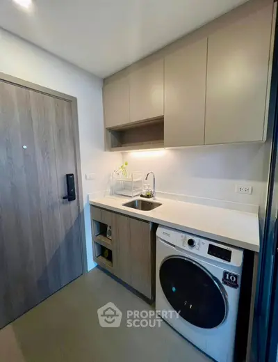 Modern kitchen with washing machine and sleek cabinetry in compact apartment