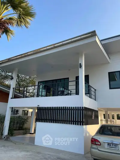 Modern two-story house with balcony and carport in a serene neighborhood.