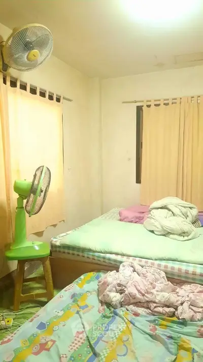 Cozy bedroom with simple decor and natural light, featuring a fan and comfortable bedding.
