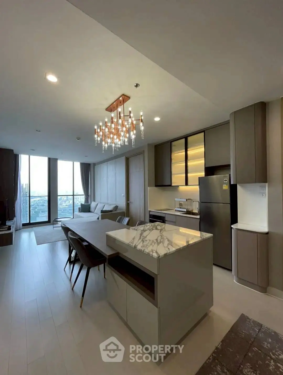Modern open-plan living room with kitchen, featuring elegant chandelier and city view.