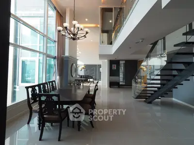Luxurious modern dining area with high ceilings and elegant staircase in a spacious open-plan layout.