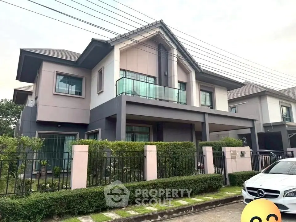 Modern two-story house with balcony and landscaped garden in suburban neighborhood.