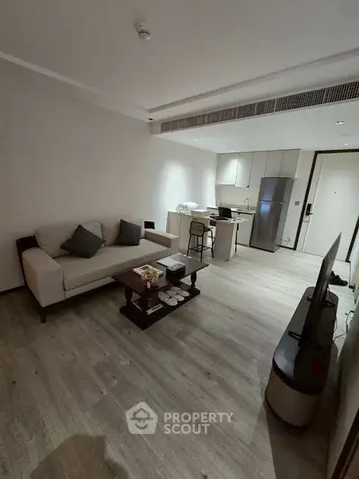 Modern living room with open kitchen, sleek furniture, and wooden flooring in a contemporary apartment.