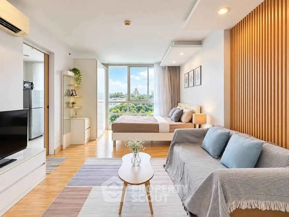 Modern open-plan living room and bedroom with stylish decor and large windows offering a scenic view.