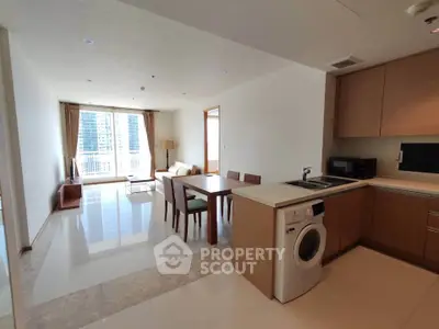 Spacious modern living room with open kitchen and washing machine, featuring large windows and elegant dining area.