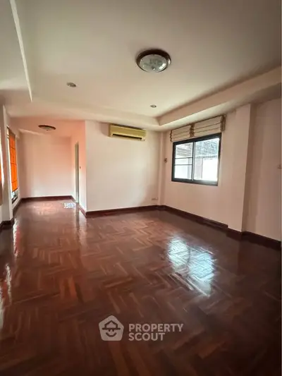 Spacious empty living room with wooden flooring and large window.