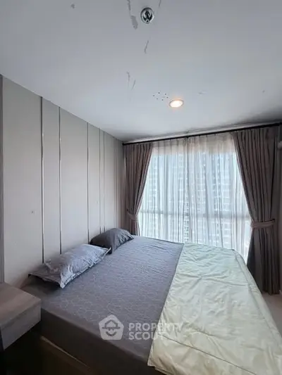 Spacious bedroom with large window and modern decor in a high-rise apartment.