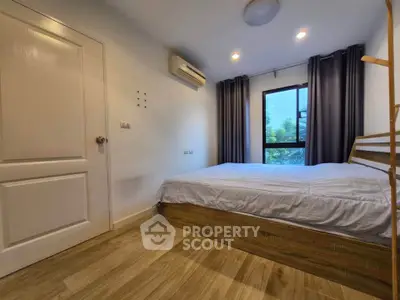 Cozy bedroom with wooden flooring, large window, and air conditioning in modern apartment.