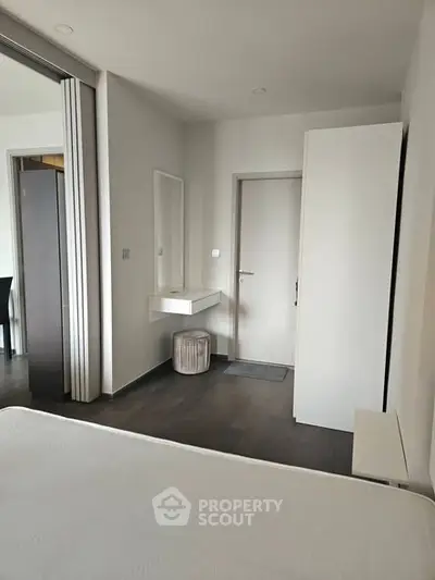 Modern minimalist bedroom with sleek white furniture and dark wood flooring.