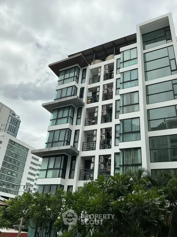Modern multi-story apartment building with large windows and lush greenery