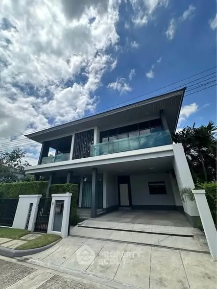 Modern two-story house with large balcony and sleek design under a bright blue sky.