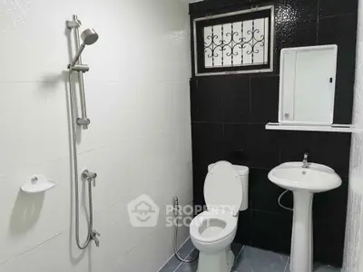 Modern bathroom with sleek black and white tiles, featuring a shower, toilet, and pedestal sink.