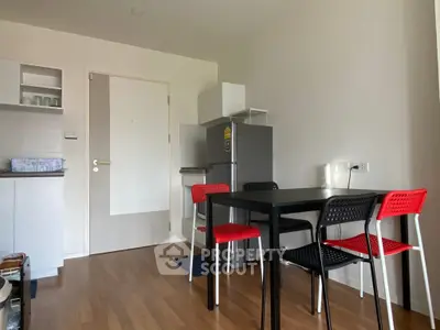 Modern kitchen with dining area featuring sleek black table and vibrant red chairs, compact fridge, and minimalist design.