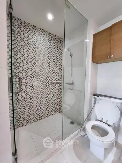 Modern bathroom with glass shower and mosaic tiles, featuring sleek fixtures and ample storage.