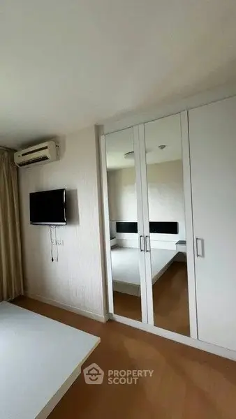 Modern bedroom with mirrored wardrobe and wall-mounted TV in a cozy apartment.
