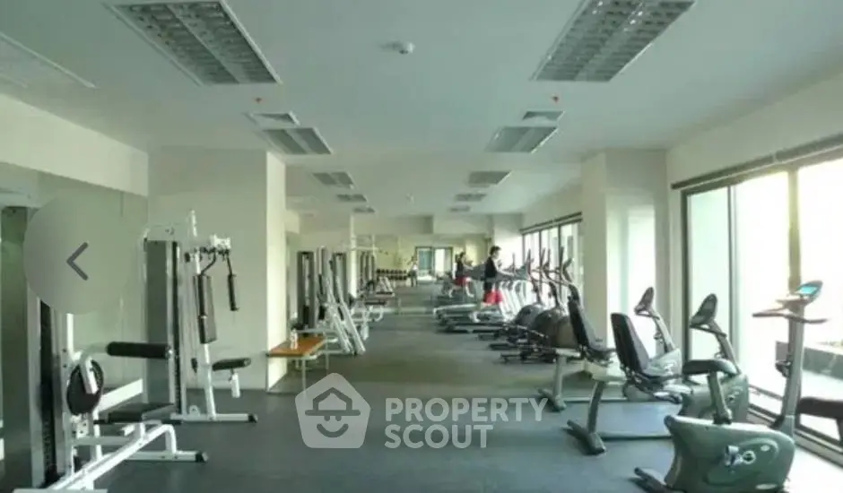 Spacious gym with modern fitness equipment and large windows in a residential building.