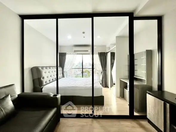 Modern bedroom with glass partition and city view, featuring stylish furniture and natural light.