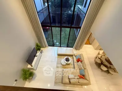 Luxurious living room with high ceilings and large windows, offering a stunning garden view.