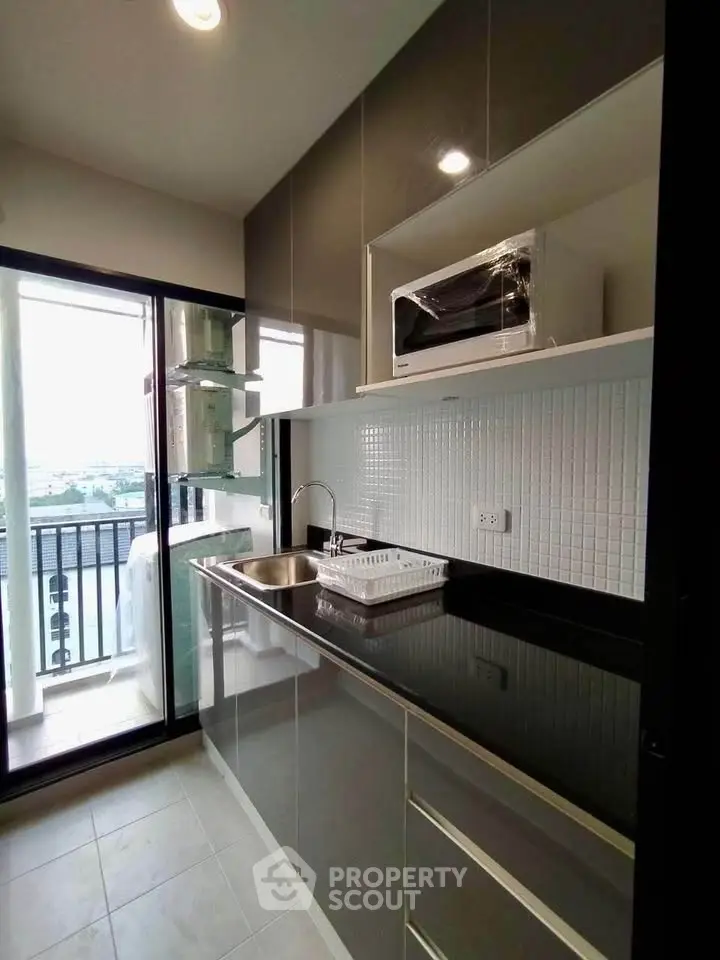 Modern kitchen with sleek cabinets and balcony view, featuring a microwave and sink.