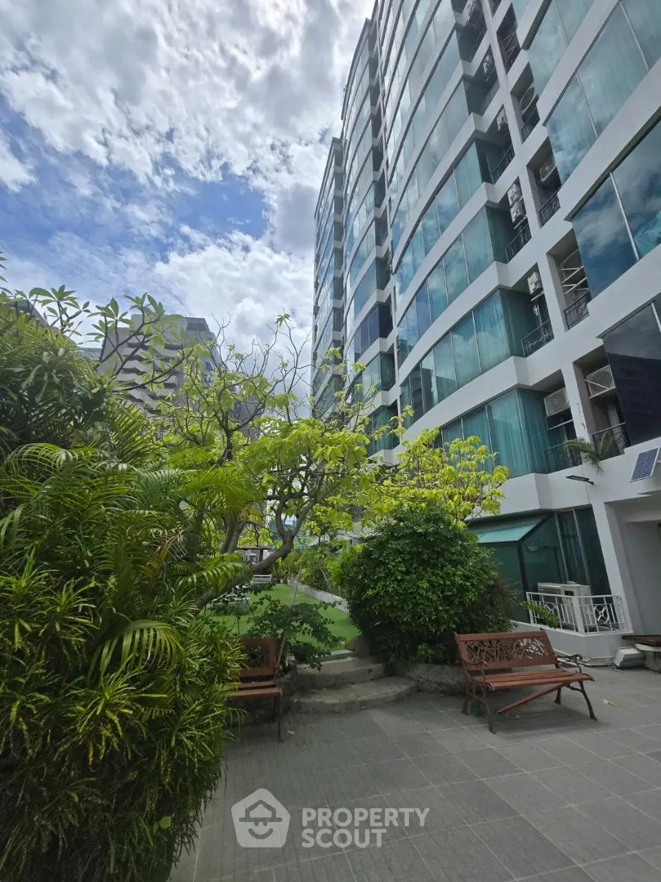 Modern high-rise building with lush garden and seating area, perfect for urban living.