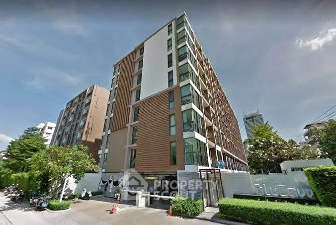 Modern multi-story residential building with lush greenery and clear blue sky.