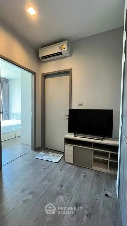 Modern apartment interior with sleek flooring and air conditioning, featuring a cozy TV area and bedroom view.