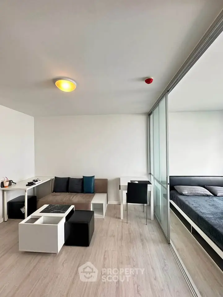 Modern living room with sleek furniture and adjacent bedroom in open layout apartment.