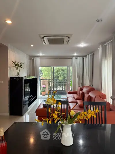 Spacious living room with red leather sofa and large windows overlooking greenery.
