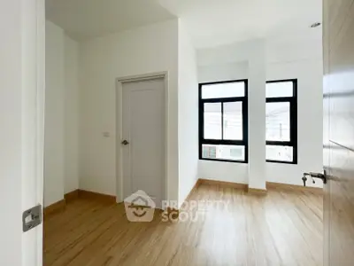 Bright empty room with wooden flooring and large windows, perfect for customization.