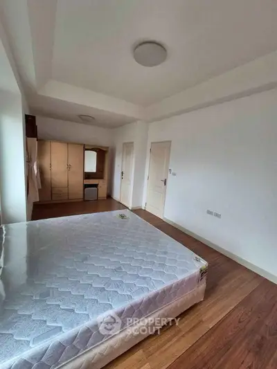 Spacious bedroom with wooden flooring and ample natural light, featuring a large bed and wardrobe.