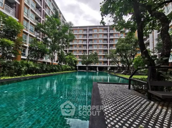 Lush greenery surrounds a tranquil pool area, offering a serene oasis amidst a modern residential complex with ample lounging spaces.