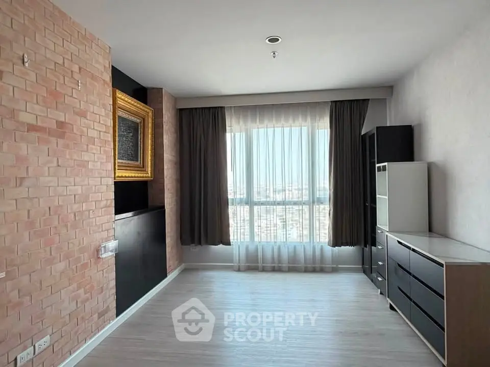 Spacious unfurnished room with large window and brick accent wall in modern apartment.