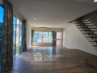Spacious living room with large windows and modern staircase in a bright, airy home.