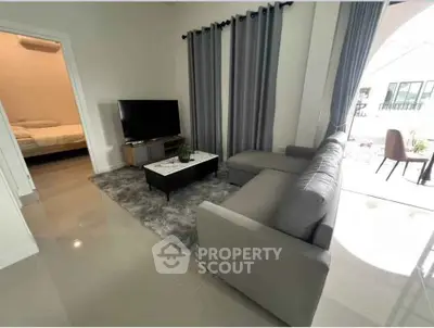 Modern living room with sleek gray sofa and large TV, adjacent to a cozy bedroom.