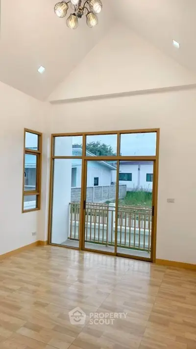 Spacious living room with high ceiling and large windows offering natural light and outdoor view.