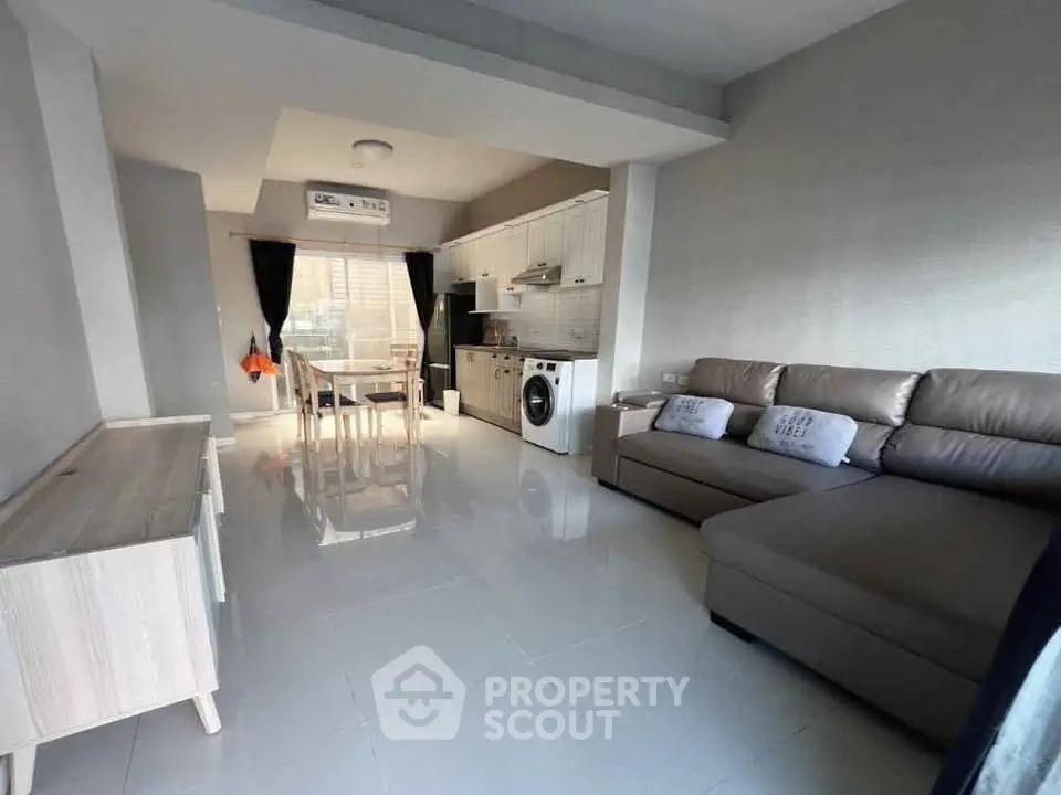 Modern open-plan living room with kitchen, featuring sleek furniture and ample natural light.