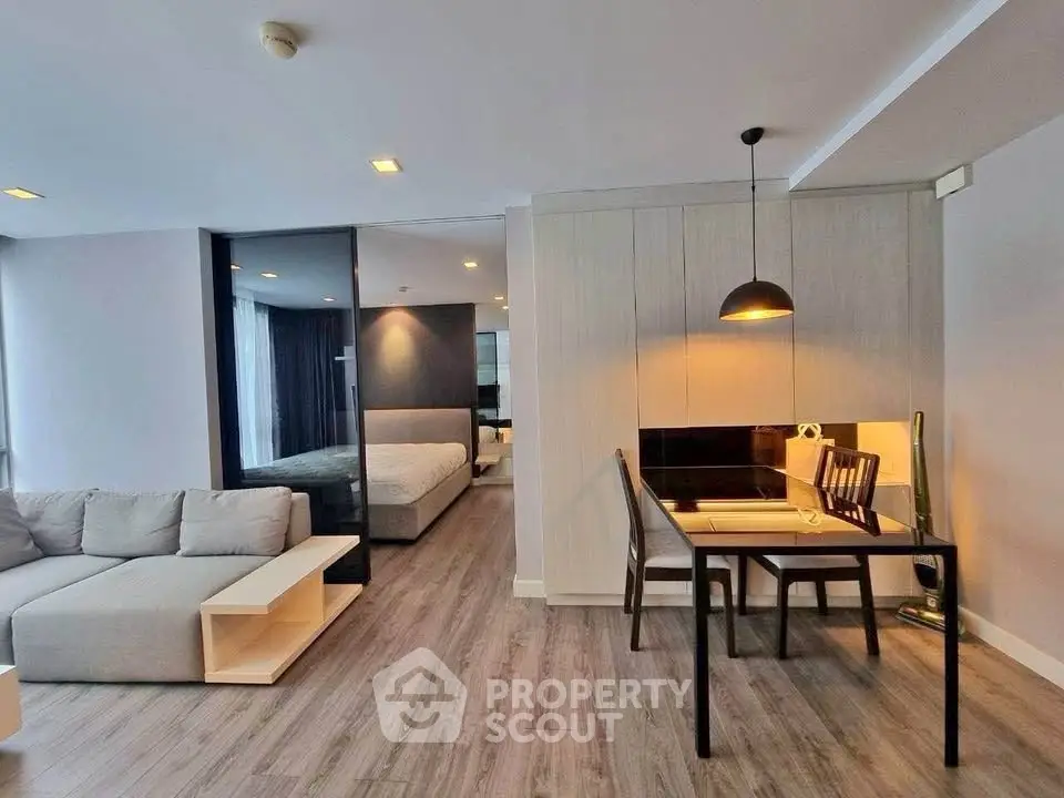 Modern open-plan living room with dining area and bedroom, featuring sleek furniture and stylish lighting.