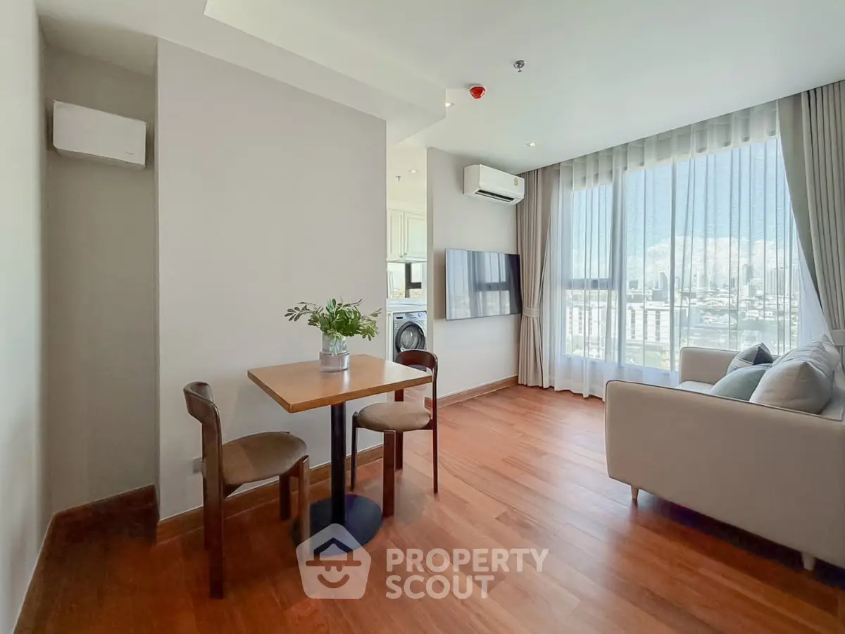 Bright living room with wooden flooring, modern furniture, and large windows offering a stunning city view.